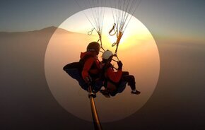 Persona volando en parapente durante un espectacular atardecer sobre el Teide, con el cielo teñido de tonos naranjas y rosados.